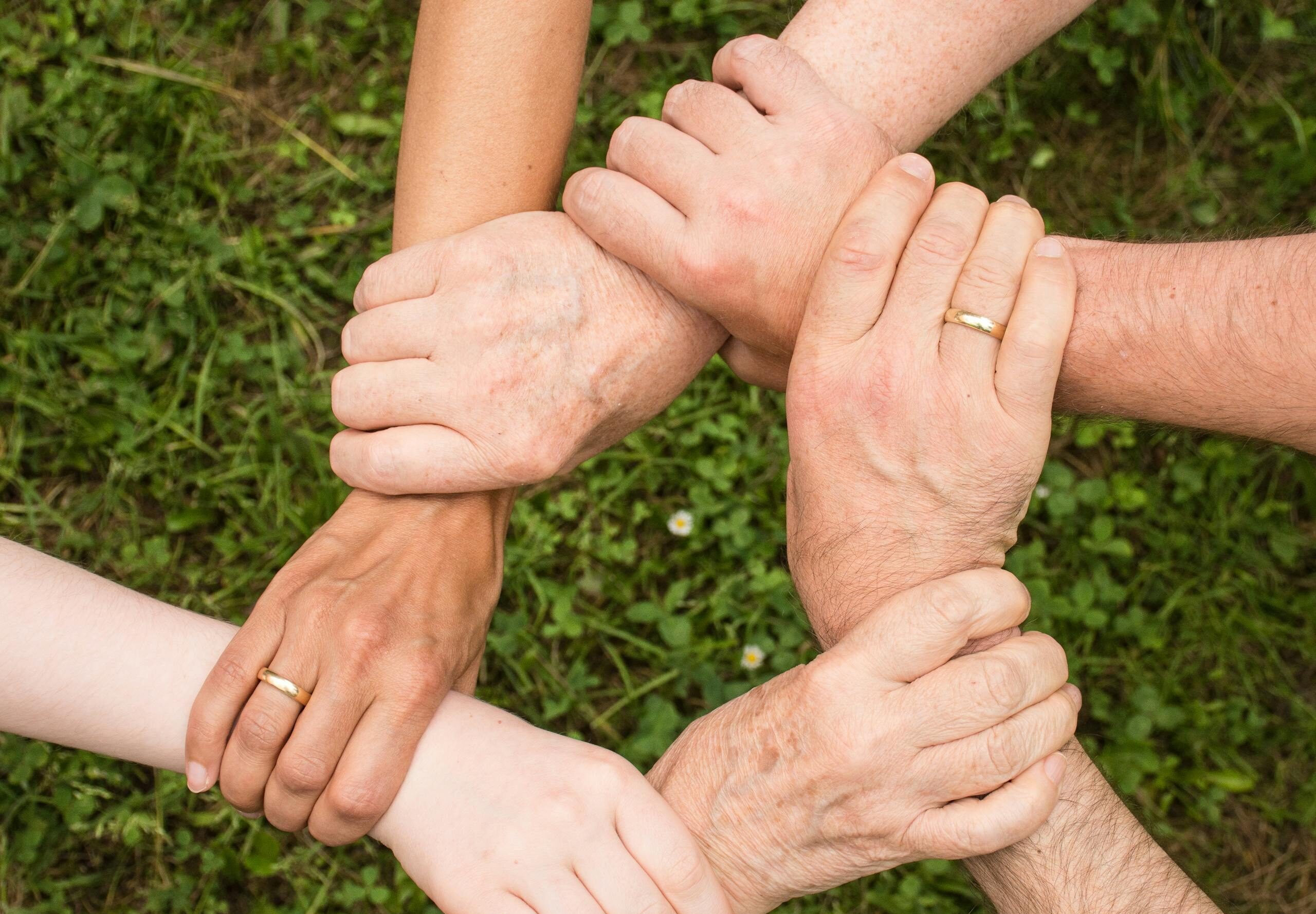 Close-up of diverse hands forming a connection, symbolizing teamwork and unity outdoors.